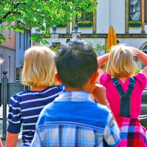 Das Bild zeigt eine Gruppe Kinder, die am Historischen Marktplatz das Alte Rathaus bestauenen. 