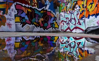 Bunte Graffiti-Kunst an einer Wand, gespiegelt in einer Wasserpfütze auf dem Boden.