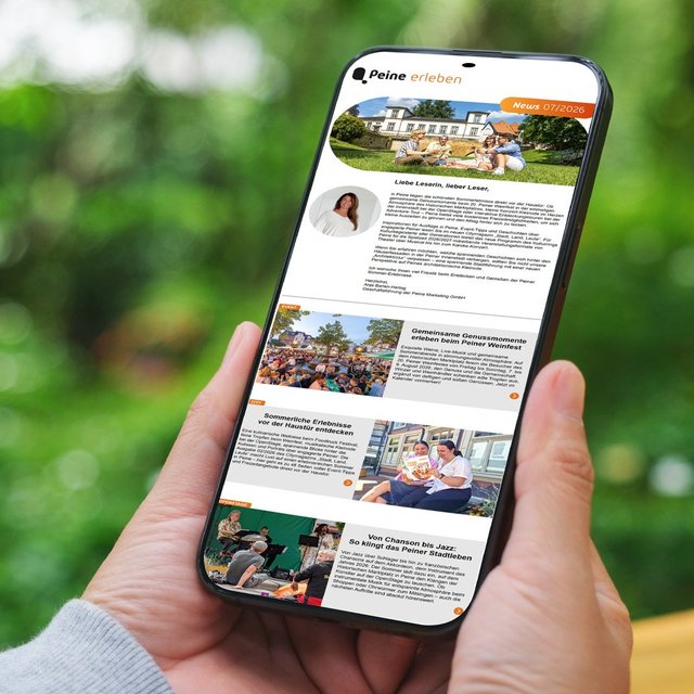 Eine Person hält ein Smartphone in der Hand. Auf dem Display ist der digitale Newsletter „Peine erleben“ geöffnet, der mit Bildern und Beiträgen zu Veranstaltungen, Freizeitangeboten und Erlebnissen in Peine gefüllt ist. Im Hintergrund ist eine unscharfe grüne Parklandschaft zu sehen.
