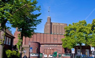 Historische Außenansicht der Härke-Brauerei Peine mit markantem Backsteinbau und dem Schriftzug „Härke-Bier“ am Turm. Die traditionsreiche Braumanufaktur ist von Bäumen eingerahmt und steht sinnbildlich für Biergenuss und Braukultur aus Peine.