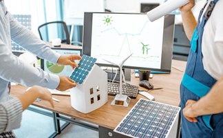 Personen arbeiten am Modell eines Hauses mit Photovoltaikmodulen.