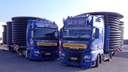 Zwei blaue Sattelzugmaschinen der Firma Fritz Bente Spedition mit großen Kabeltrommeln auf den Aufliegern.