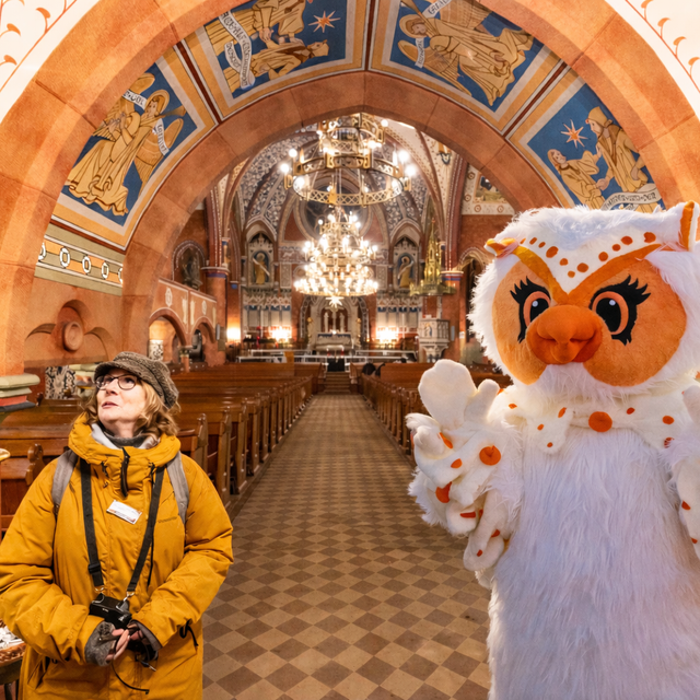 Uhlinchen in der St.-Jakobi-Kirche Peine neben einer Stadtführerin, Blick auf das kunstvoll bemalte Kirchenschiff mit Bögen und Kronleuchtern.