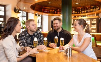 Freunde genießen frisch gezapftes Bier an einem Holztisch in einer gemütlichen Bar in Peine – entspannte Atmosphäre, angeregte Gespräche und moderne Gastronomie im Herzen der Stadt.