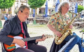 Zwei Musiker spielen Gitarre und Saxophon bei der OpenStage auf dem Historischen Marktplatz in Peine vor Cafés und Fachwerkhäusern.
