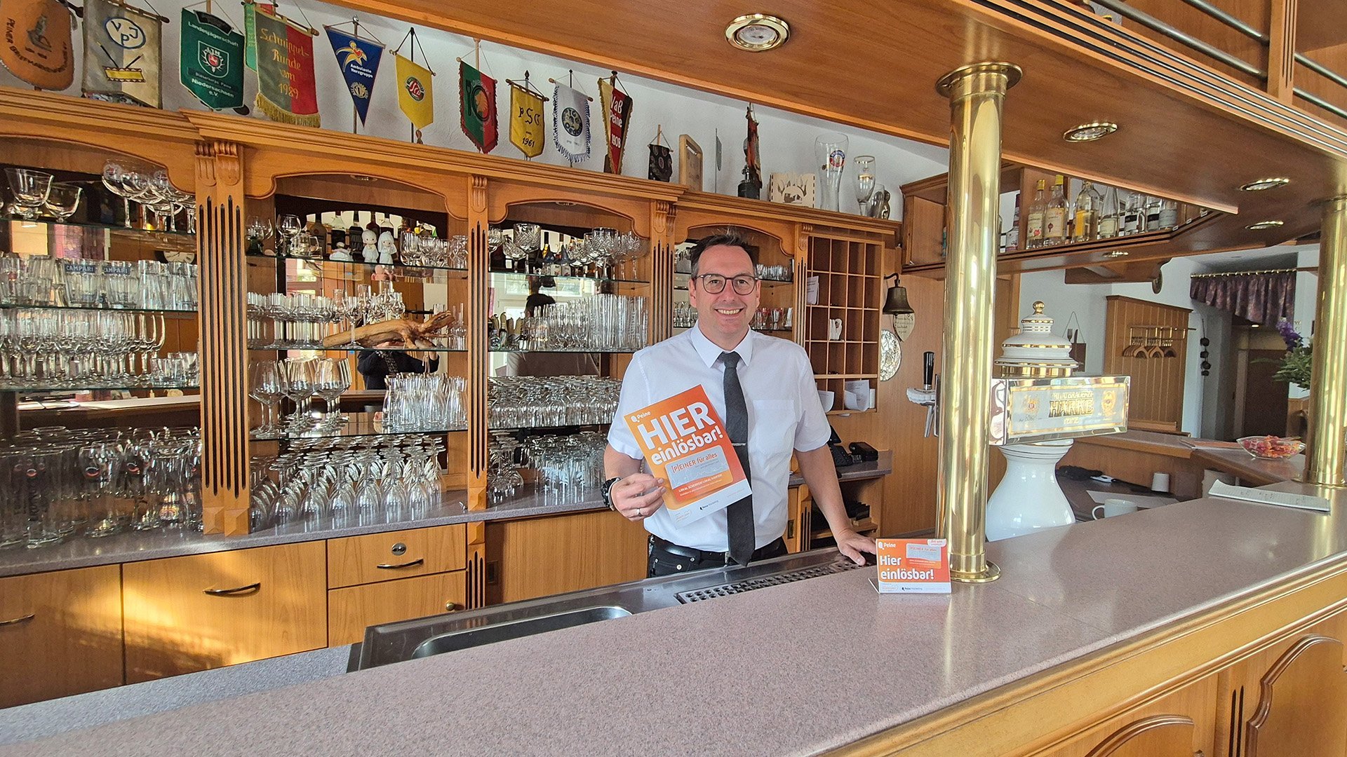 Ein Mann steht hinter einer Bar und hält ein orangefarbenes Schild mit der Aufschrift „HIER kostenlos“.