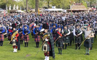 Großes Highland Gathering mit hunderten Dudelsackspielern in traditionellen Kilts, die gemeinsam auf einer Wiese musizieren, umgeben von zahlreichen Zuschauerinnen und Zuschauern bei einem schottischen Kulturfest.