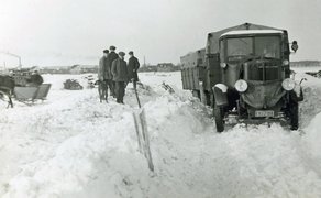 Ein Lkw mit Planenaufbau auf einer verschneiten Straße, daneben stehen mehrere Männer.