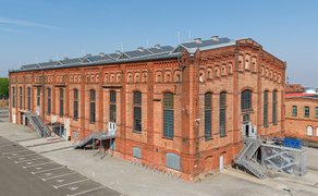 Großes Backsteingebäude einer ehemaligen Industrieanlage mit hohen Fenstern und Außentreppen.