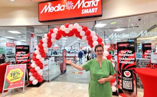 Eingangsbereich des neuen MediaMarkt SMART in der City Galerie Peine mit rotem Ballonbogen zur Eröffnung. Vor dem Markt begrüßt ein Mitarbeiter die Besucher des kompakten Elektronikfachmarkts.