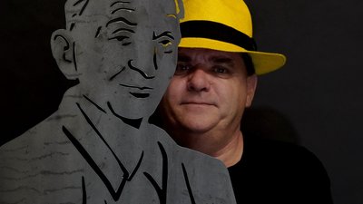 Porträt einer Person mit gelbem Hut neben einer metallenen Figuren-Silhouette als künstlerische Installation im urbanen Stadtraum der Stadt Peine, Symbol für Kreativität, Identität und zeitgenössische Stadtmarke.