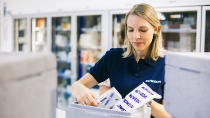 Eine Frau sortiert Medikamentenpackungen in eine graue Kühlbox.
