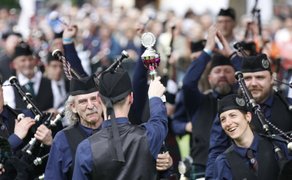 Siegerehrung beim Highland Gathering in Peine: Dudelsackspieler einer Pipes-&-Drums-Band feiern jubelnd den Gewinn eines Pokals, während das Publikum im Hintergrund applaudiert.