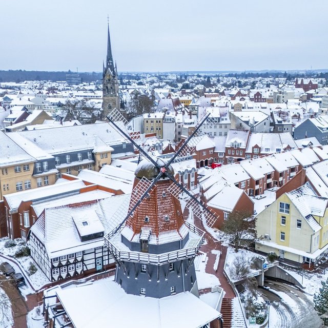 Luftaufnahme der verschneiten Innenstadt von Peine mit historischer Windmühle, Kirche und schneebedeckten Dächern im Winter.