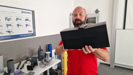 Ein Mann hält einen schwarzen Kunststoffquader in der Größe eines Ziegelsteins in die Kamera.