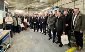 Gruppe von Personen in einer Industriehalle, einige tragen Anzug.