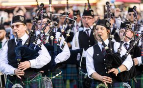 Mehrere Musiker in schottischer Tracht spielen auf Dudelsäcken vor einer Menschenmenge.