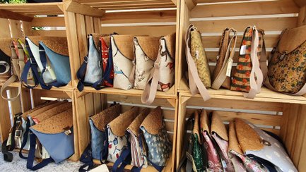 Regal aus Holzkisten mit handgefertigten Taschen aus Korkmaterial in verschiedenen Formen und Mustern.