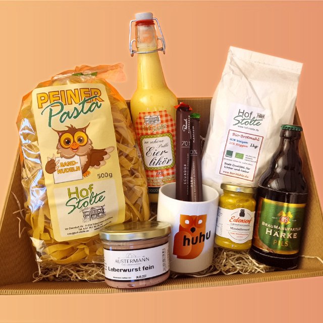 Geschenkkorb mit Pasta, Eierlikör, Aufstrichen in Glasdosen, Dose, Tasse und Bierflasche auf Holzwolle in Karton