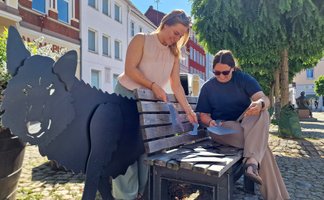 Peiner Projekte von der Initiative Stadtimpulse ausgezeichnet: Zwei Frauen puzzeln Metallteile an einer Bank mit Wolfsfigur.