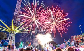 Feuerwerk beim Peiner Freischießen über dem Festplatz mit Fahrgeschäften, Lichtern und jubelndem Publikum in der Abenddämmerung.