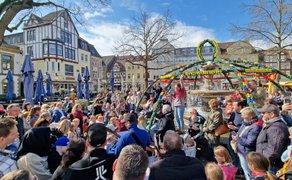 Menschenmenge um einen festlich mit bunten Eiern geschmückten Brunnen auf einem historischen Marktplatz mit Fachwerkhäusern im Hintergrund.