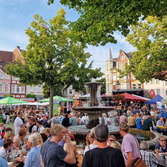 Viele Menschen sitzen und stehen beim Peiner Weinfest rund um einen Brunnen auf einem Marktplatz.