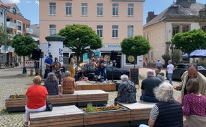 Das Bild zeigt das Publikum, das vor der OpenStage auf der Stadtoase auf dem Historischen Marktplatz in Peine Platz genommen hat. 