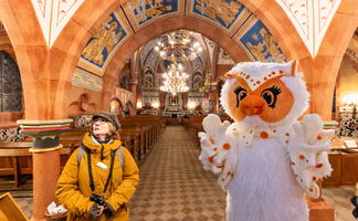 Uhlinchen in der St.-Jakobi-Kirche Peine neben einer Stadtführerin, Blick auf das kunstvoll bemalte Kirchenschiff mit Bögen und Kronleuchtern.