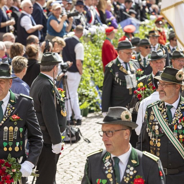 Menschen in Schützenuniformen laufen mit Blumensträußen und Fahnen durch eine volle Straße während eines Festumzugs.