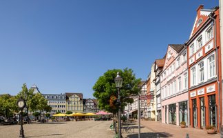 Blick über den Marktplatz in der Peiner Innenstadt mit historischen Fachwerkhäusern, Cafés, Bäumen und Kopfsteinpflaster bei sonnigem Wetter