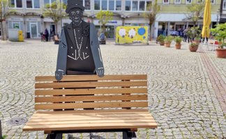 Das Bild zeigt eine  Bank mit Skulptur auf dem Historischen Marktplatz in Peine, was als Kunst im öffentlichen Raum gilt. 