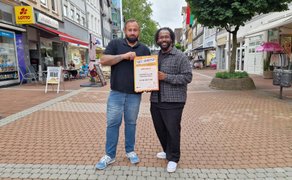 Zwei Männer stehen in der Peiner Fußgängerzone und halten gemeinsam eine GetStarted-Urkunde für das Start-up „WIE BEI MUTTERN“ in die Kamera.