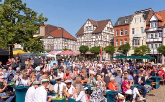 Besucher sitzen und stehen auf dem historischen Marktplatz in Peine und verfolgen ein Jubiläumsprogramm