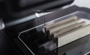 Messmaschine mit drei rechteckigen grauen Proben auf einer Glasplatte unter einem Messsensor.