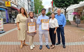 Fünf Personen stehen in der Peiner Fußgängerzone. Zwei von ihnen halten GetStarted-Urkunden für die Geschäftsideen „AILA“ und „Tutor Network“ in die Kamera.