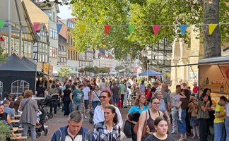 „Belebte Fußgängerzone in einer deutschen Innenstadt mit zahlreichen Passanten, Außengastronomie, Geschäften und begrünten Bereichen.“