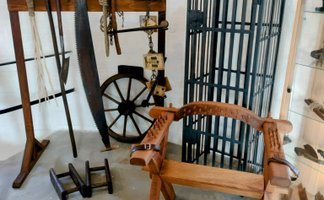 Ausstellung historischer Folterinstrumente mit Holzgestell, Säge, Seilen, Streckbank und Eisenkäfig in einem Museumsraum, die die Methoden der Justiz zur Zeit der Hexenverfolgung veranschaulichen.