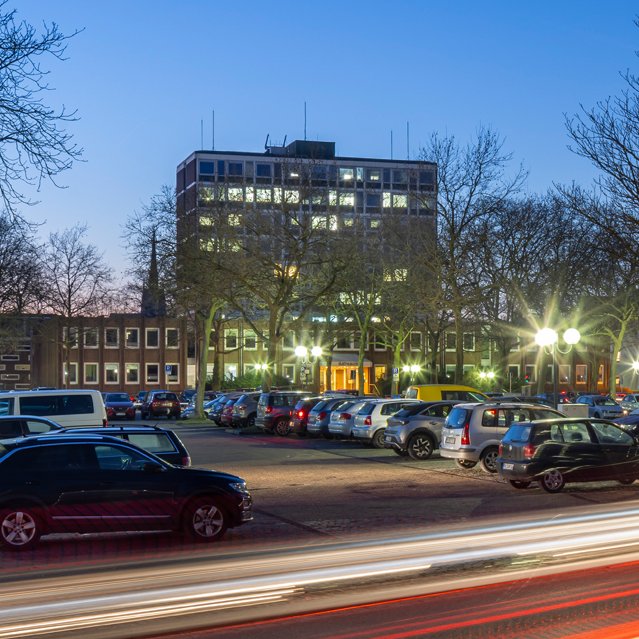 Das Bild zeigt den Schützenplatz in Peine als Parkplatz mit einigen Autos in den Abendstunden. 