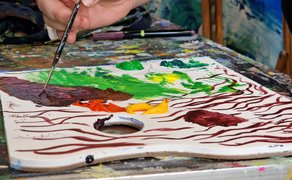Eine Hand tupft einen Pinsel auf eine Malerpalette mit Farbmischungen.