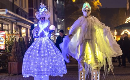 Leuchtende Walking-Acts in futuristischen Kostümen bei einer Abendveranstaltung in der Innenstadt von Peine, mit beleuchteten Kleidern und Stelzen.