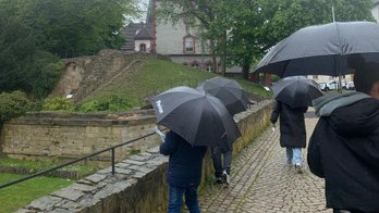 Das Bild zeigt Menschen die einen Regenschirm tragen von hinten. 