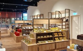 Modern gestalteter Verkaufsraum im Rausch Schokoladenhaus Peine mit hellen Holzregalen und übersichtlich präsentierten Schokoladen- und Süßwarenprodukten. Die klare Struktur und warme Materialien unterstreichen den hochwertigen Genuss- und Einkaufscharakter der Chocolaterie in Peine.