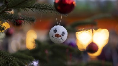 Weihnachtsbaum mit einer weißen Kugel, die ein lachendes Gesicht mit schwarzem Mund und roten Wangen zeigt, und einer roten Kugel im Hintergrund.