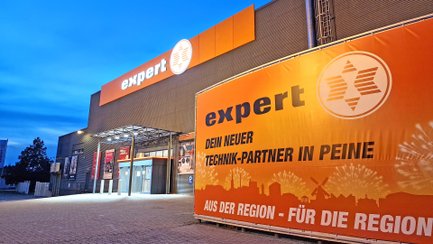 Außenansicht des expert-Elektromarkts in Peine bei Dämmerung. Die orange beleuchtete Fassade zeigt den Schriftzug „expert“ und den Eingang des Marktes.