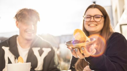 Junge Menschen genießen Eis in einem Café in Peine und halten eine Eisschale mit Waffel in die Sonne – entspannte Stimmung in der Innenstadt.