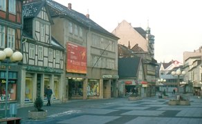 Eine Fußgängerzone mit Fachwerkhäusern, Laternen mit Kugellampen und Pflanzkübeln, einzelne Passanten gehen die Straße entlang.