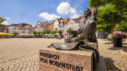 Das Bild zeigt die sitzende Skulptur des Friedrich von Bodenstedt auf dem Historischen Marktplatz in Peine. 