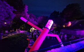 Leuchtende aufblasbare Tanzfigur blickt auf die Silent Disco im Schlosspark Peine, während zahlreiche Besucher bei Nacht mit Funkkopfhörern unter farbig beleuchteten Bäumen feiern.