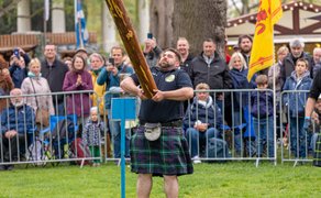 Teilnehmer im Kilt wirft Baumstamm beim Highland Game „Tossing the Caber“ vor Publikum im Peiner Stadtpark